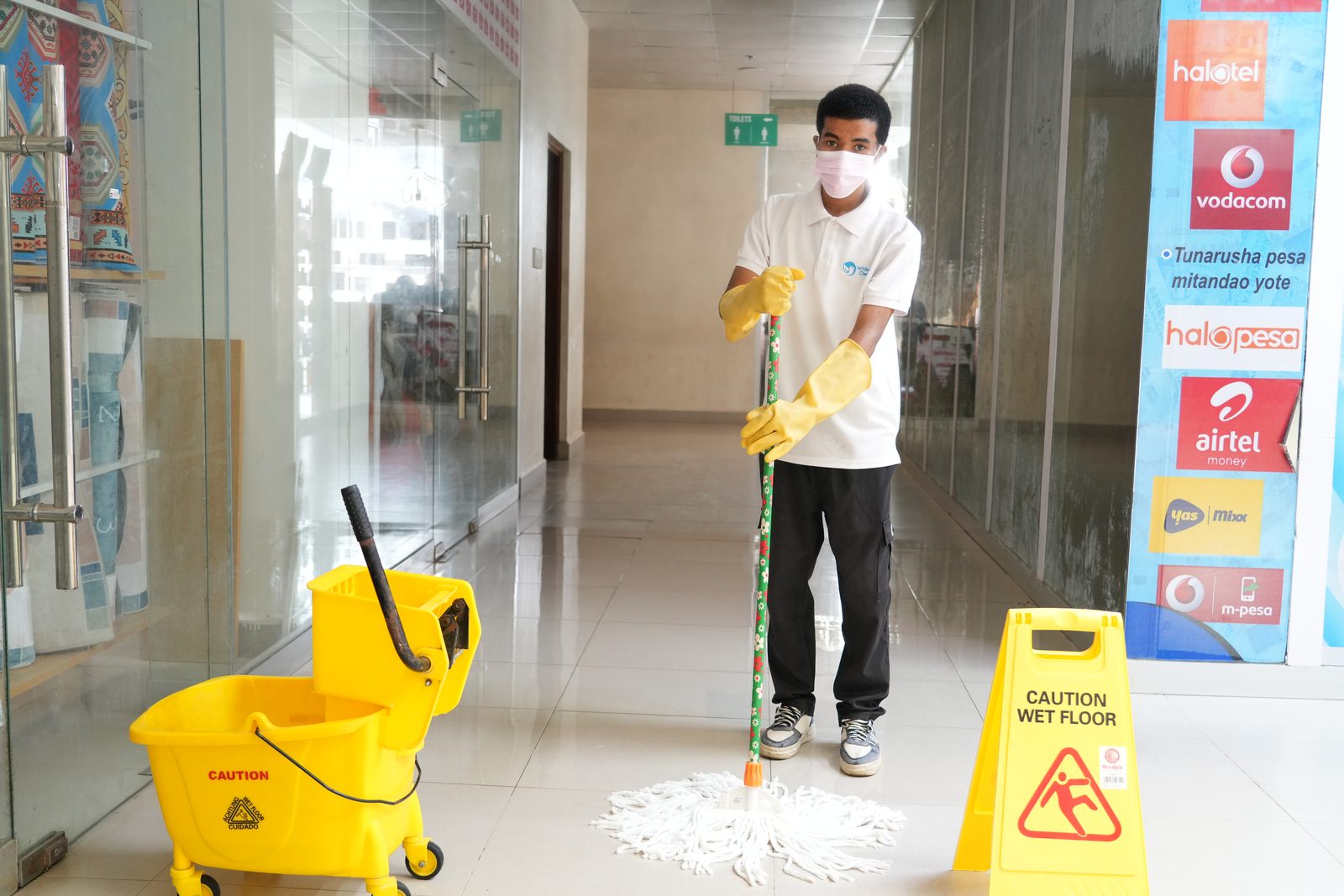 WhiteBird cleaner with a mop beside a wet-floor caution sign in an office corridor